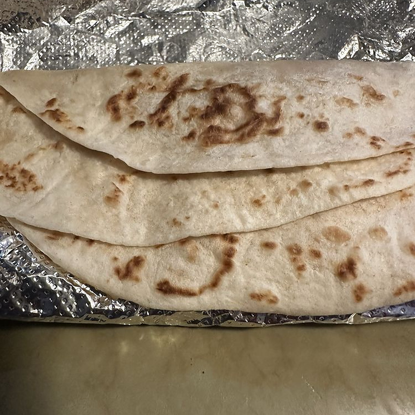 Three flour tortillas folded on foil at the counter